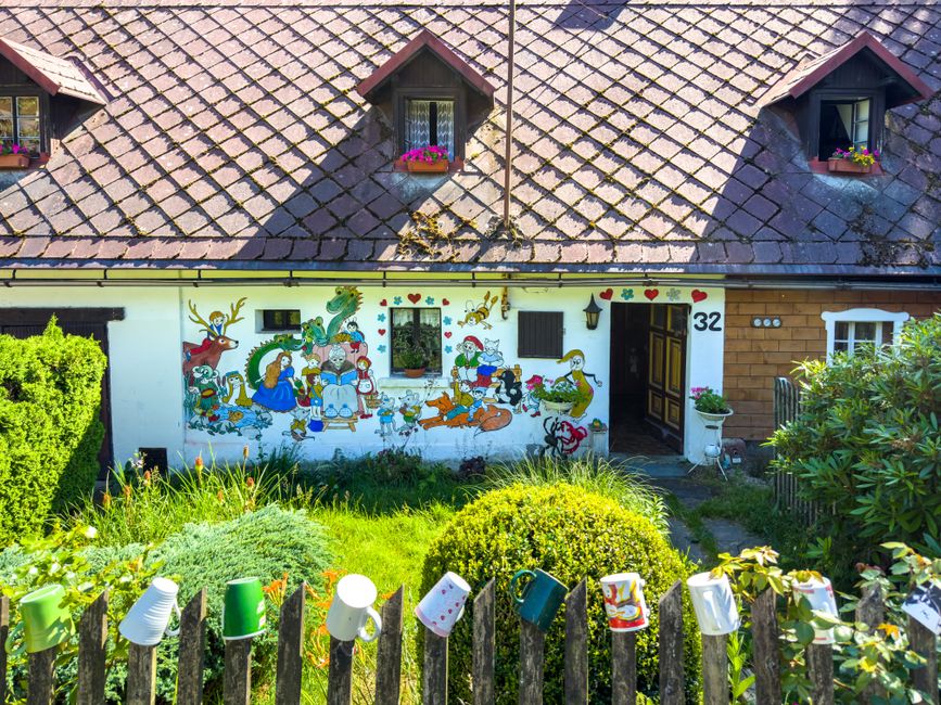 Small painted house with a mural and flowers in the yard.