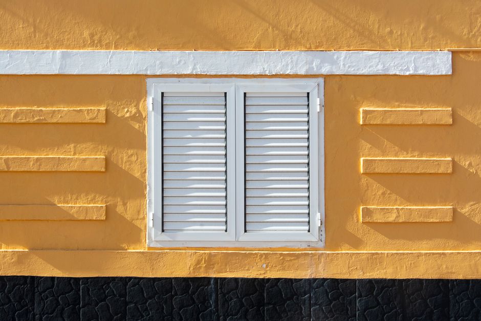 Close view of a yellow painted wall with white shutters.